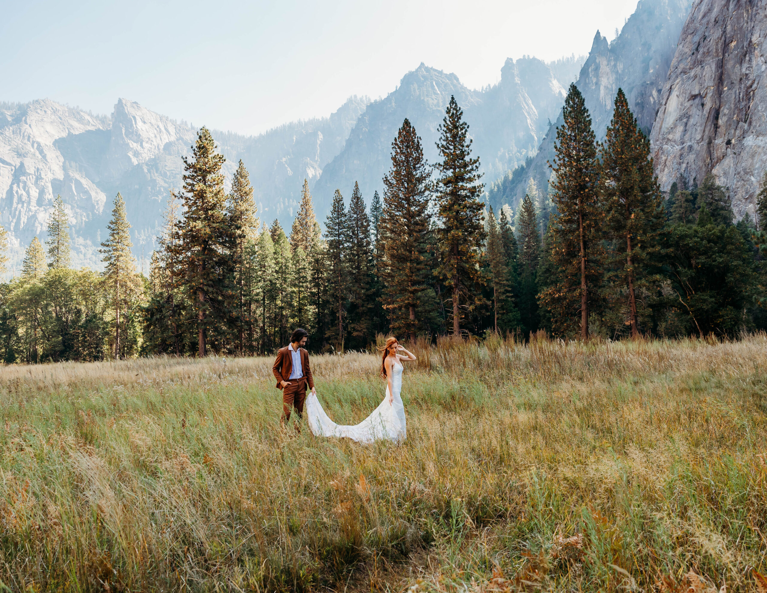 Bride and groom embracing in El Capitan Meadow during their Yosemite elopement with mountain views and tall pine trees in the background.