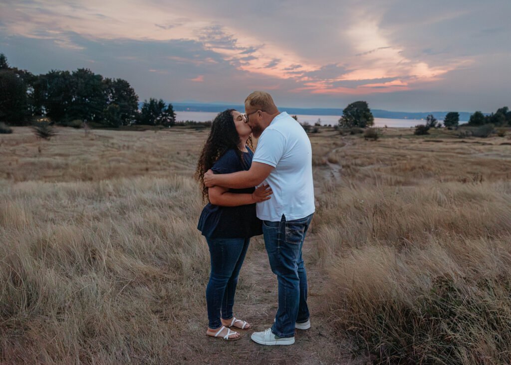 Interracial couple walking through a golden meadow at Discovery Park in Seattle with soft sunset colors in the sky.