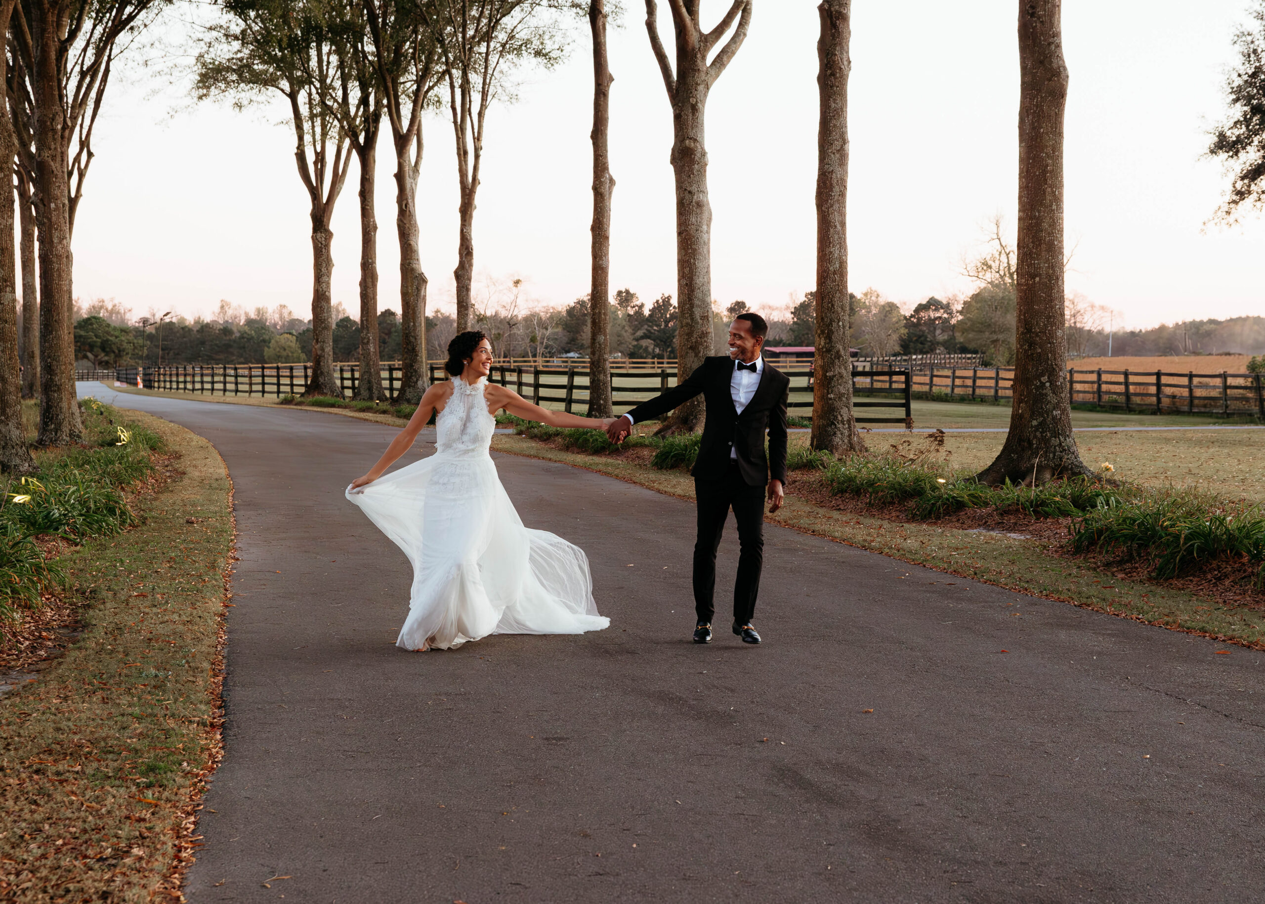 Bride and groom walking on tree lined road during North Carolina wedding at Britton Manor with romantic countryside backdrop