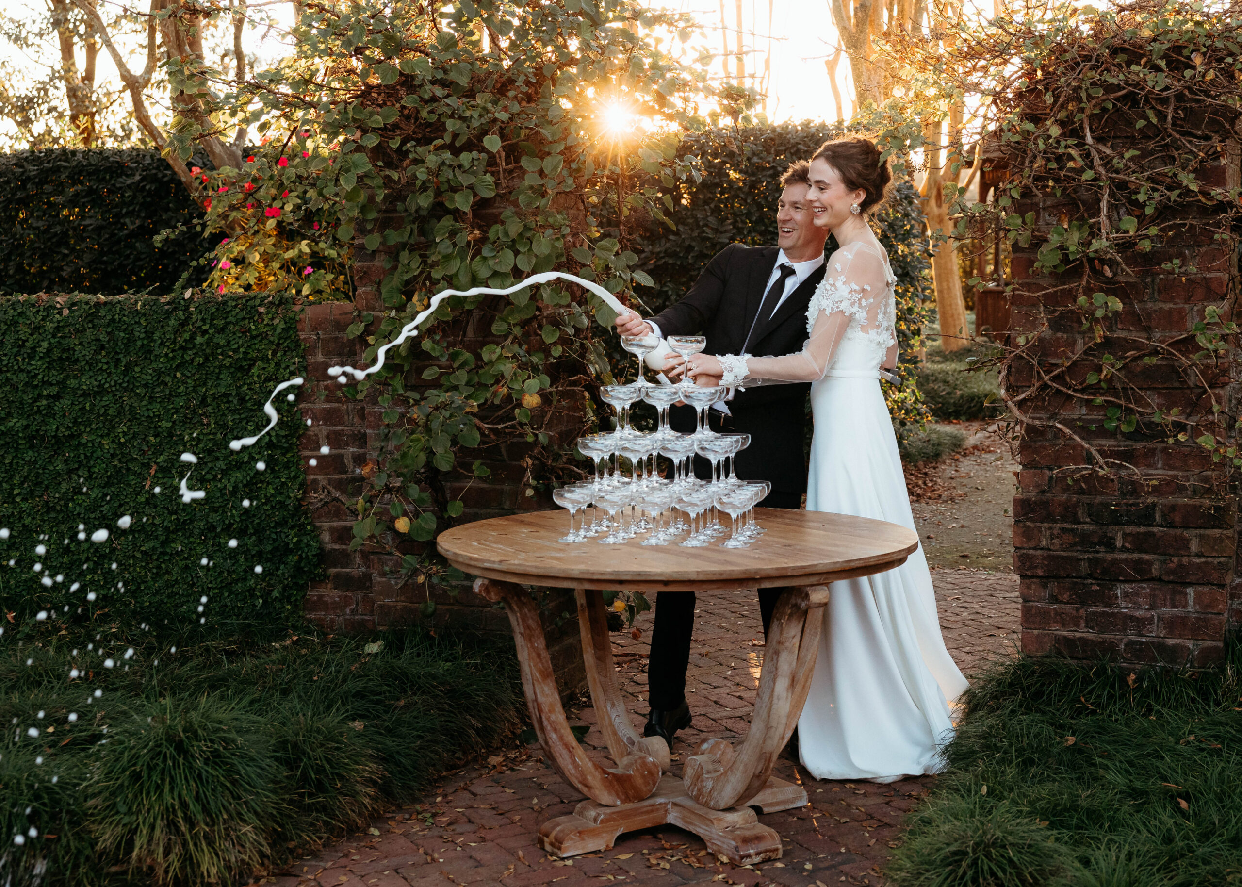 Couple pouring champagne tower during North Carolina wedding at Britton Manor in garden setting with golden hour sunlight